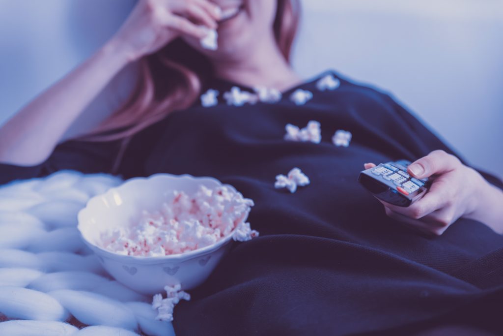 Woman watching TV eating popcorn.